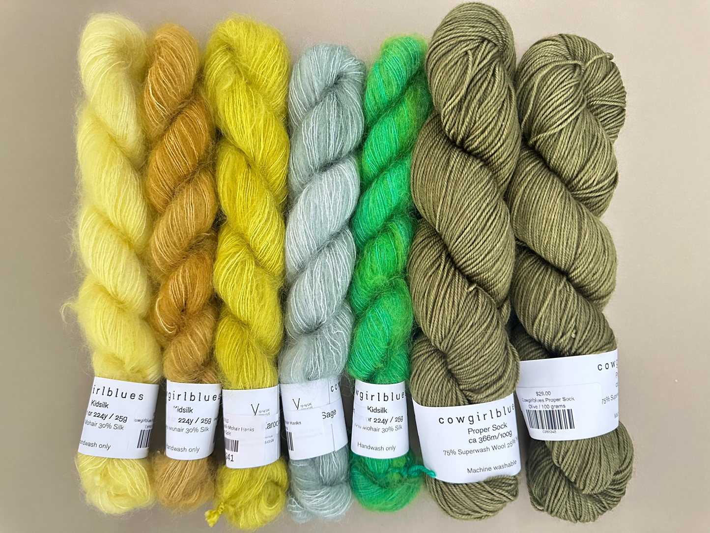 Five skeins of yarn in green, yellow, and gray with labels on a beige background